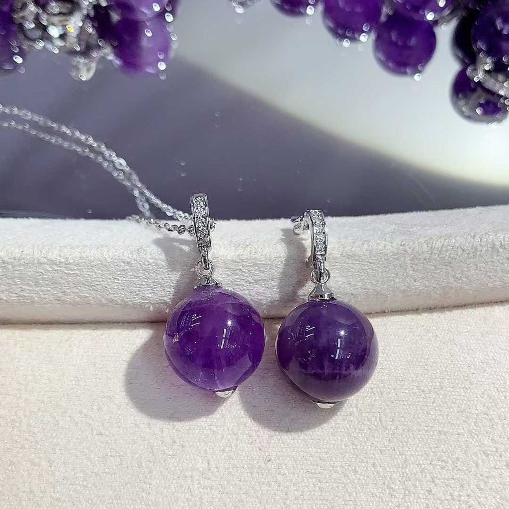 Two round purple pendants with silver-tone fittings displayed side by side on a white cushion