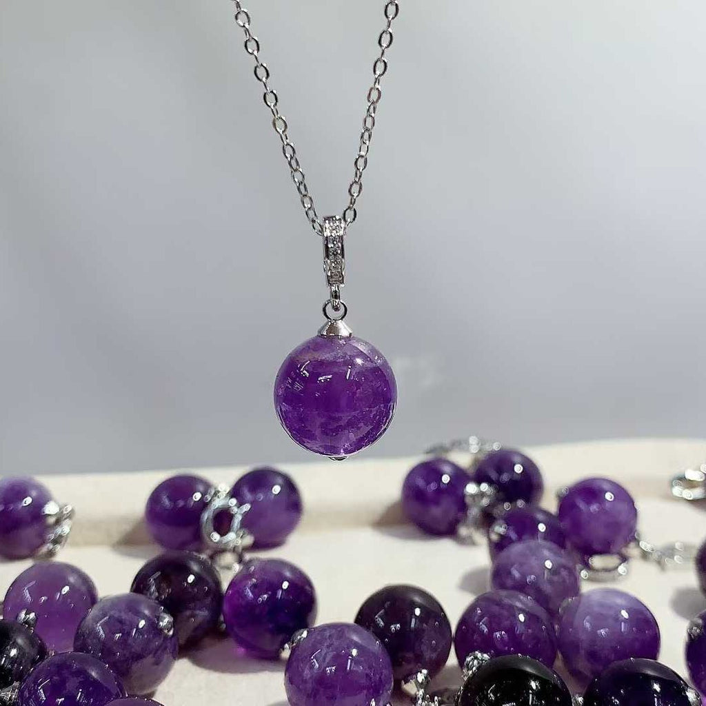 Close-up of a round purple pendant on a silver-tone chain with more purple pendants below.