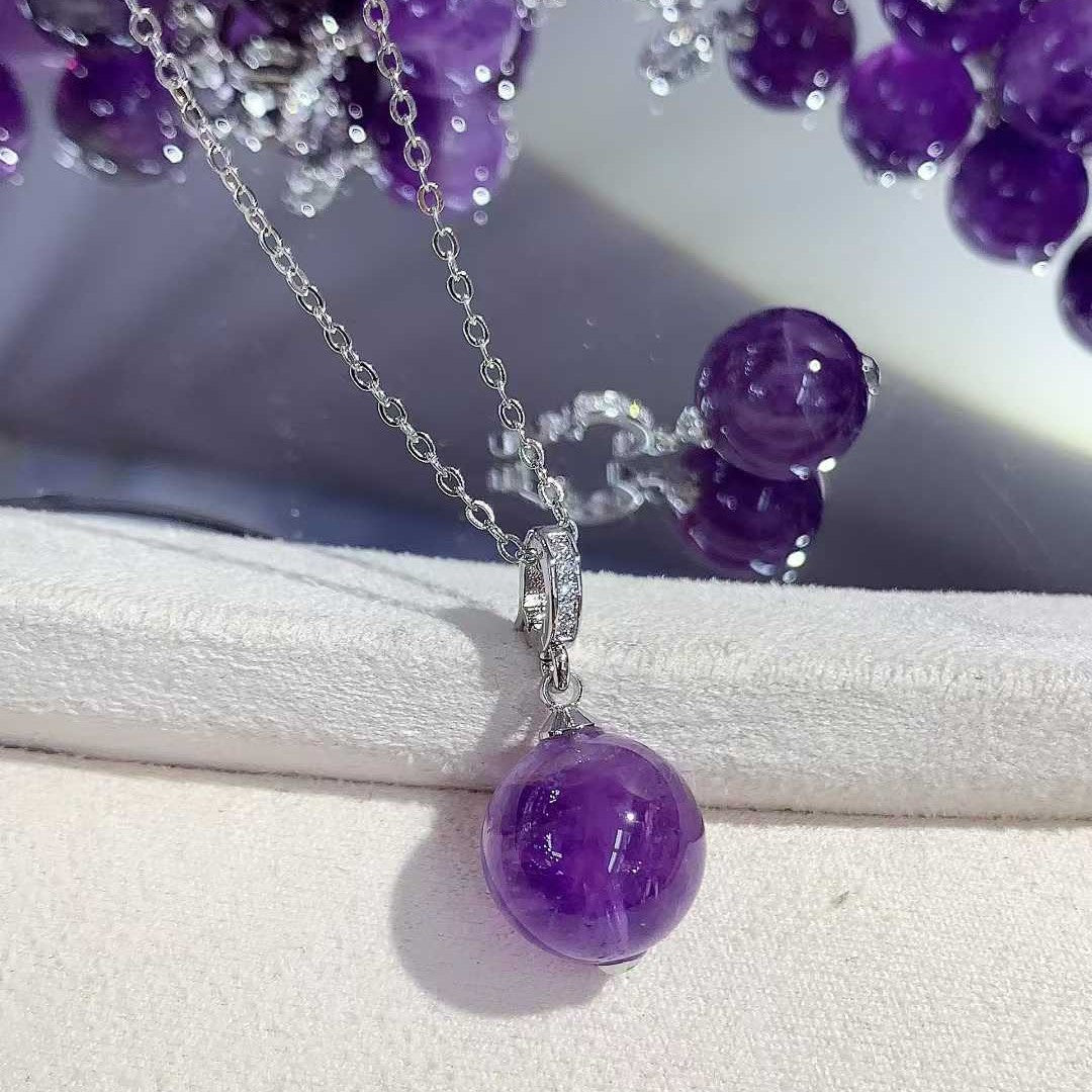 “Purple round pendant on a silver-tone chain resting on a white jewelry display.”