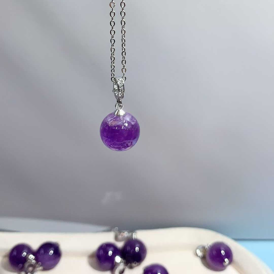 Purple round pendant hanging from a silver-tone chain against a gray background